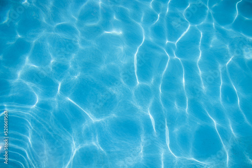 ripples of water from a swimming pool with a blue background with the sun reflecting in the water