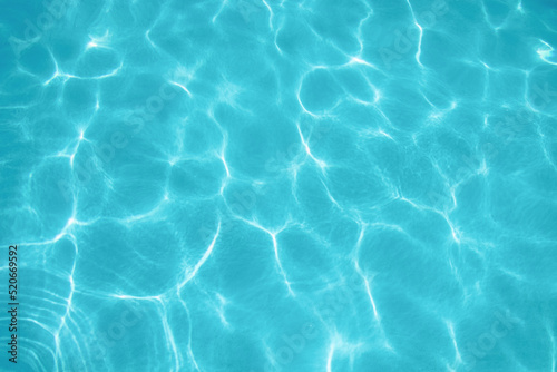 ripples of water from a swimming pool with a blue background with the sun reflecting in the water