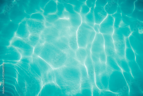 ripples of water from a swimming pool with a blue background with the sun reflecting in the water © Lorena