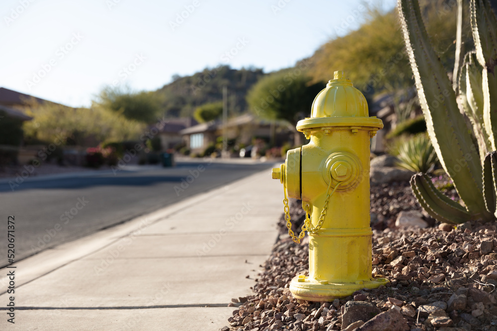Yellow fire hydrant on bed of pebbles next to a street sidewalk in suburban neighborhood Yellow fire hydrant on bed of pebbles next to a street sidewalk in suburban neighborhood