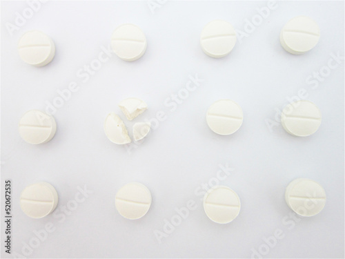            Round white medical pills arranged in square order and one of them is crushed into four parts. Pill splitting.                        