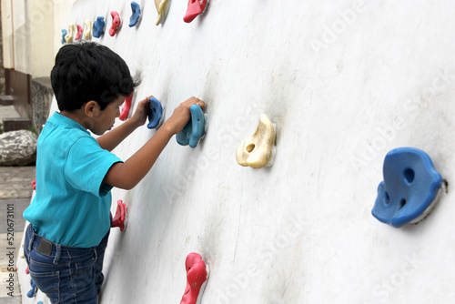 Latin dark-haired male child with blue t-shirt practicing sports wall climbing without fear of heights and exercising 
