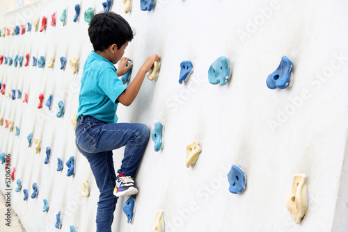 Latin dark-haired male child with blue t-shirt practicing sports wall climbing without fear of heights and exercising 