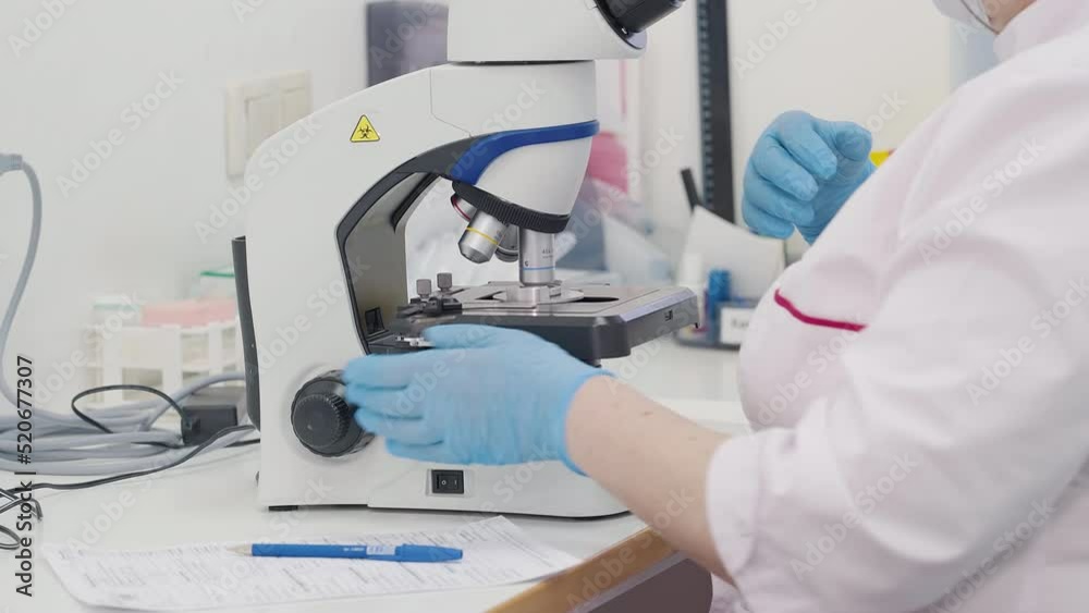 Microscope Used By Scientist To Diagnose Disease. Scientist Analyzing Blood Smear Under Microscope. Checking Blood Sample For Disease. Scientist Writes Disease Examination Result. Optical Microscope Microscope Used By Scientist To Diagnose Disease. Scientist Analyzing Blood Smear Under Microscope. Checking Blood Sample For Disease. Scientist Writes Disease Examination Result. Optical Microscope