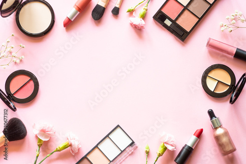 Makeup professional cosmetics on pink background with flowers. Flat lay with copy space.
