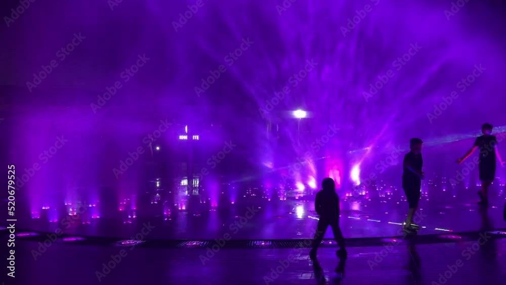 People are in the public dancing fountain at night People are in the public dancing fountain at night