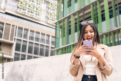 a Latin young adult woman with glasses is surprised while looking at the phone