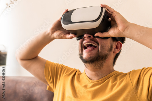 A Latin mid-adult man is wearing a VR Headset and he is looking up, sitting on the sofa