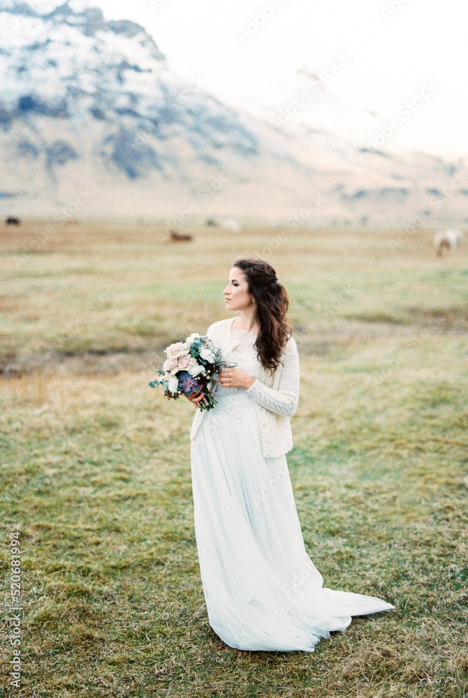 Bride with a bouquet of flowers on a pasture in a mountain valley. Iceland