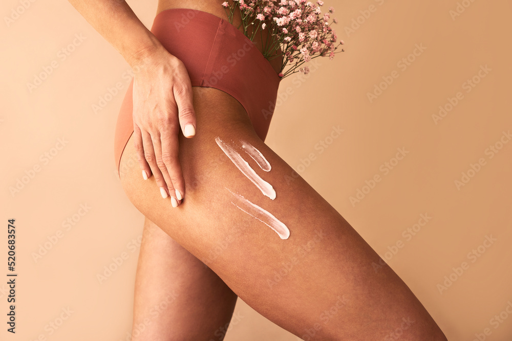 Fototapeta premium Cropped image of woman in lingerie applying cream to legs. Skin care.