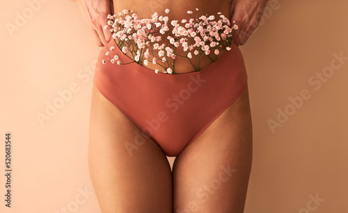 Cropped image of woman in lingerie with flowers made of panties on beige background.