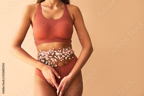   Cropped image of woman posing in lingerie with flowers made of panties on beige background. photo