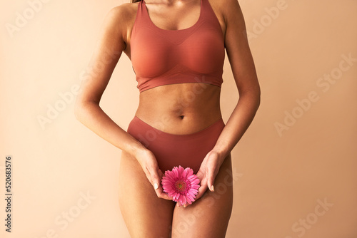 Cropped image of woman in lingerie holding pink flower on beige background. Women's health, cosmetology. photo