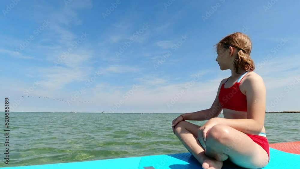 Teenage girl sitting and thinking on sup board in sea at summer holidays Teenage girl sitting and thinking on sup board in sea at summer holidays
