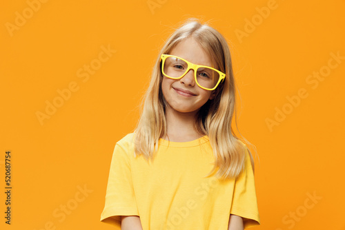 portrait of a cute beautiful school-age girl in yellow glasses for vision on a yellow background, pleasantly smiling looking at the camera © Tatiana