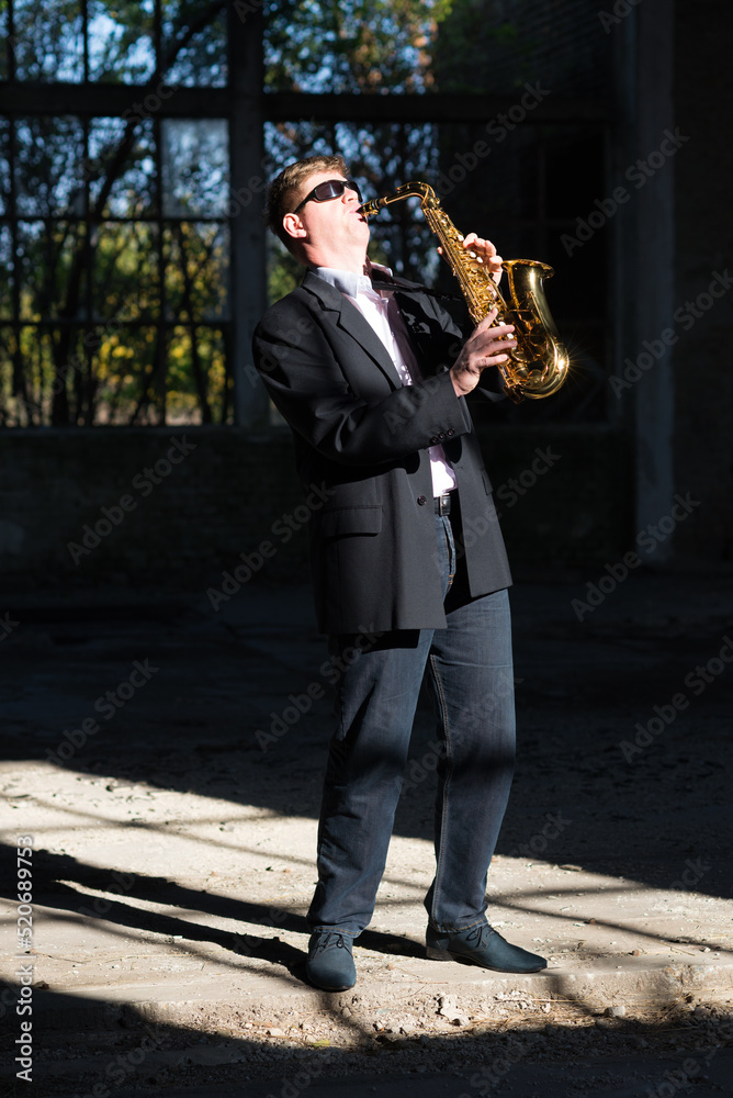 Fototapeta premium Man playing jazz on saxophone in the abandoned factory building on a sunny summer day