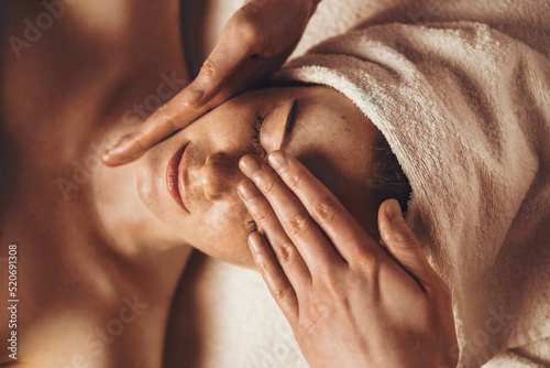 Top view of smiling freckled woman relaxing during myofascial massaging therapy at spa salon. Face massage at spa salon. Doctor hands. Pretty female patient