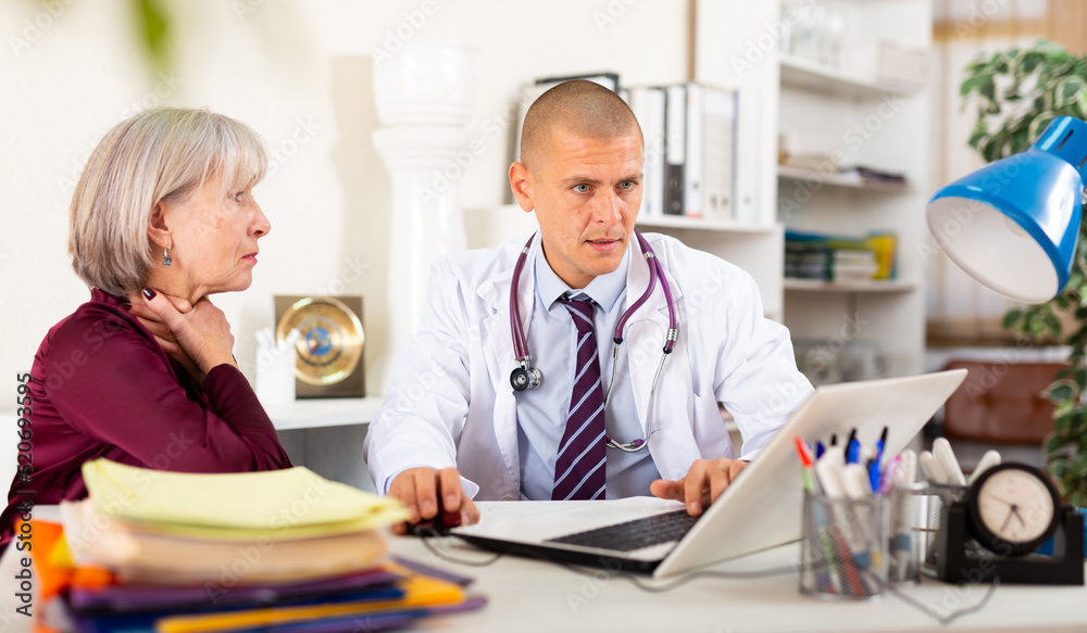 Fototapeta premium Senior woman complaining about sore throat to male doctor during medical consultation.