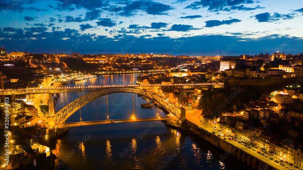 Night aerial view of Dom Luis I Bridge over Douro river against backdrop of lighted Porto city, Portugal ..