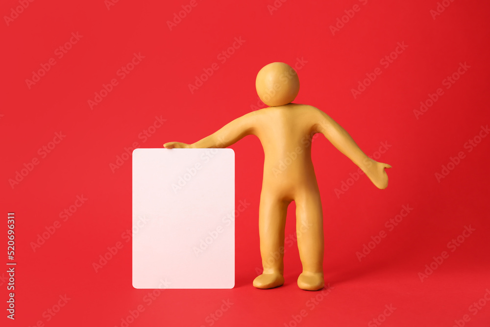 Human figure made of yellow plasticine holding blank sign on red background Human figure made of yellow plasticine holding blank sign on red background