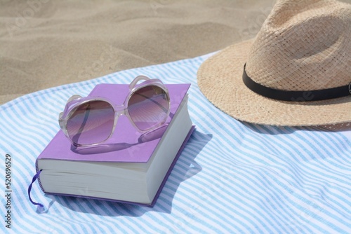 Beach towel with book, sunglasses and straw hat on sand