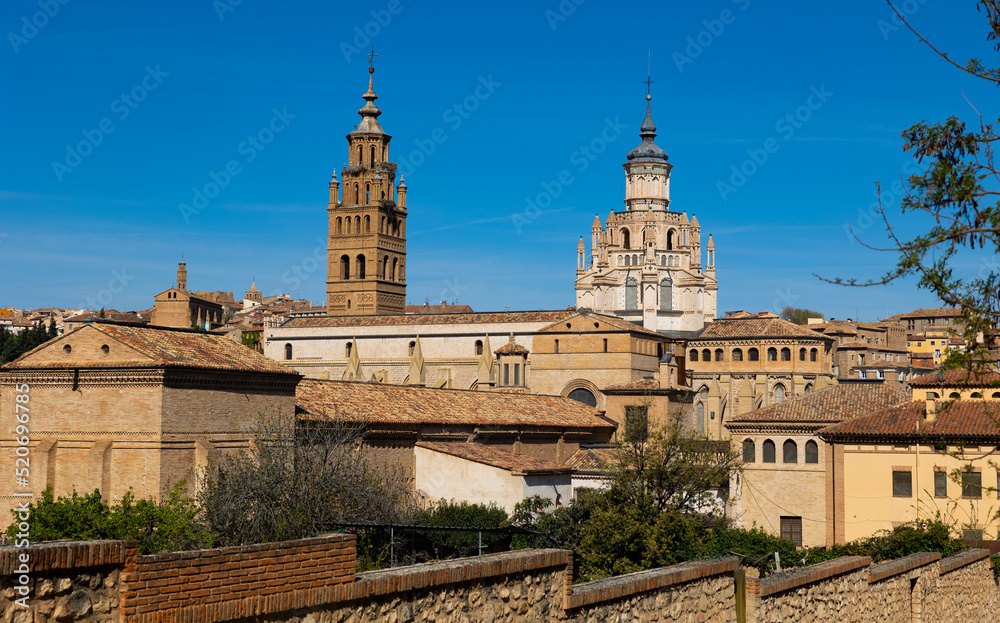 Obraz premium View of bell tower and dome of ancient Roman Catholic Cathedral rising above old residential buildings of historic quarter of Tarazona city against blue cloudless sky on sunny spring day, Spain..