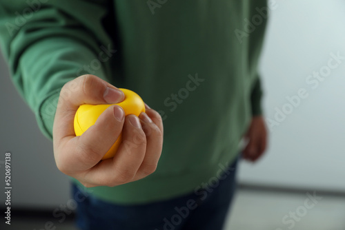 Man squeezing yellow stress ball indoors, closeup photo