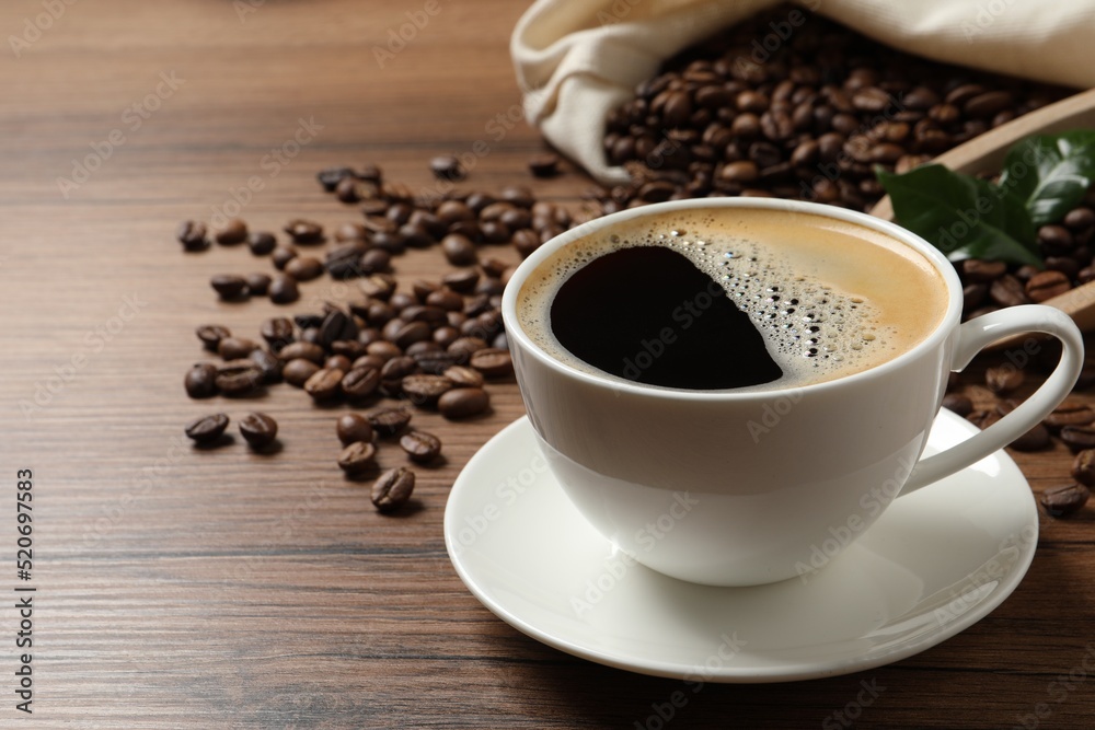 Cup of aromatic hot coffee and beans on wooden table, space for text Cup of aromatic hot coffee and beans on wooden table, space for text