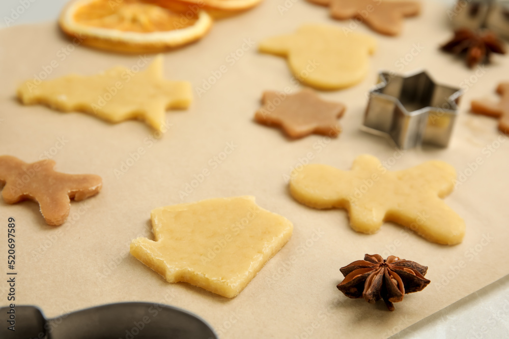 Unbaked cookies and cutters on parchment paper, closeup. Christmas biscuits