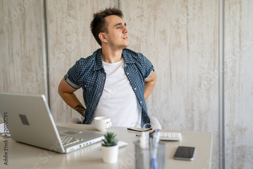 young man stretching at work while sitting at desk having back pain