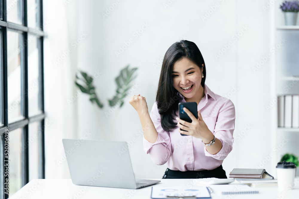 Excited happy business woman looking at phone screen, Cheerful young Asian woman using smartphone and receiving good news from the message on mobile chat application. Excited happy business woman looking at phone screen, Cheerful young Asian woman using smartphone and receiving good news from the message on mobile chat application.