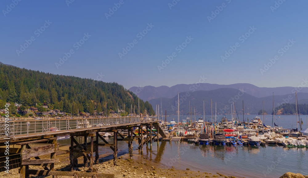 Boats moored near pier and beach at beautiful Deep Cove, BC, on a sunny day, with water-view homes in background.