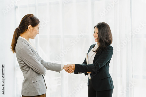 Two success business women shaking hands together, standing in the office.