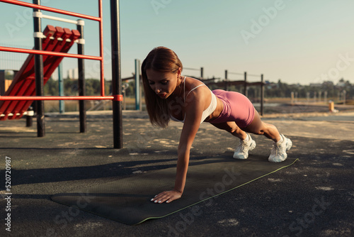 Attractive blonde in shorts doing push-ups on the sports ground. Beautiful young athletic woman doing crossfit outdoors. girl doing arm exercises
