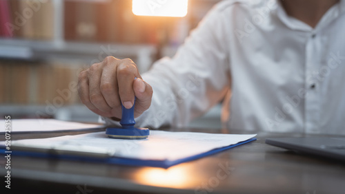 Business person man wearing a white shirt stamp seal into the contract document on the table in the office.