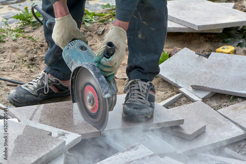 A worker with a circular saw cuts a tile in close-up.
