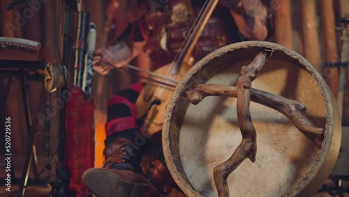 Man plays igil bow instrument on stage focus on shamanic tambourine closeup. Altai music traditions conservation. Ritual sound and inspiring show photo