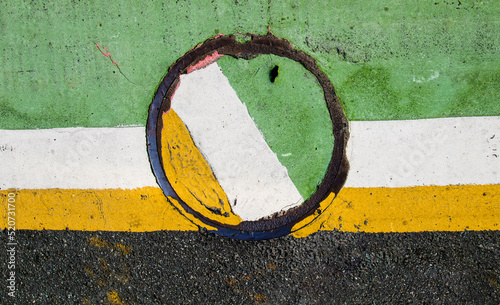 Manhole, painted in green white and yellow seen in the asphalt. Abstract background of manhole