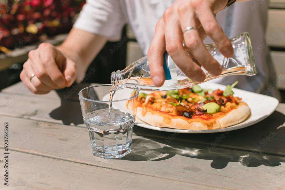 Close up of man pouring still water into glass while having launch on summer terrace. Close up of man pouring still water into glass while having launch on summer terrace.