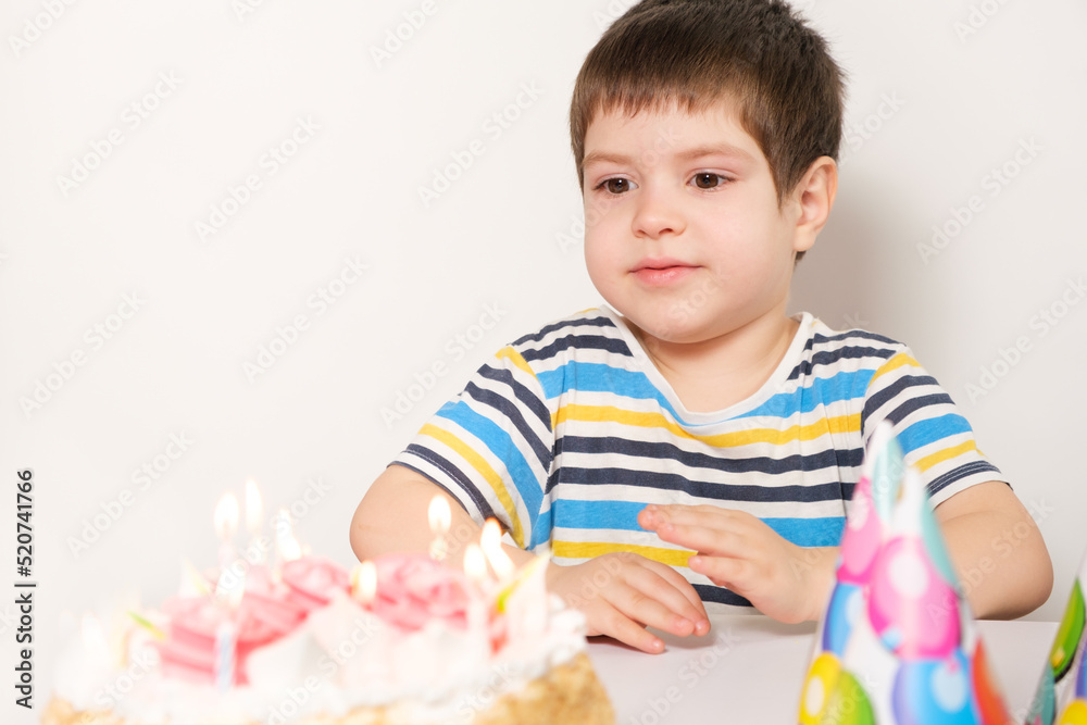 A handsome boy celebrates a birthday, sits in front of a cake with candles and makes a wish A handsome boy celebrates a birthday, sits in front of a cake with candles and makes a wish