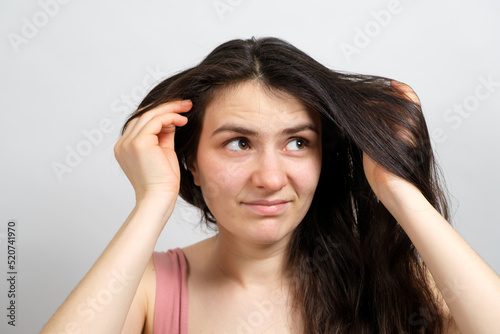 A beautiful brunette woman with long hair on a white background holds her hands on her head and thinks about what hairstyle to do