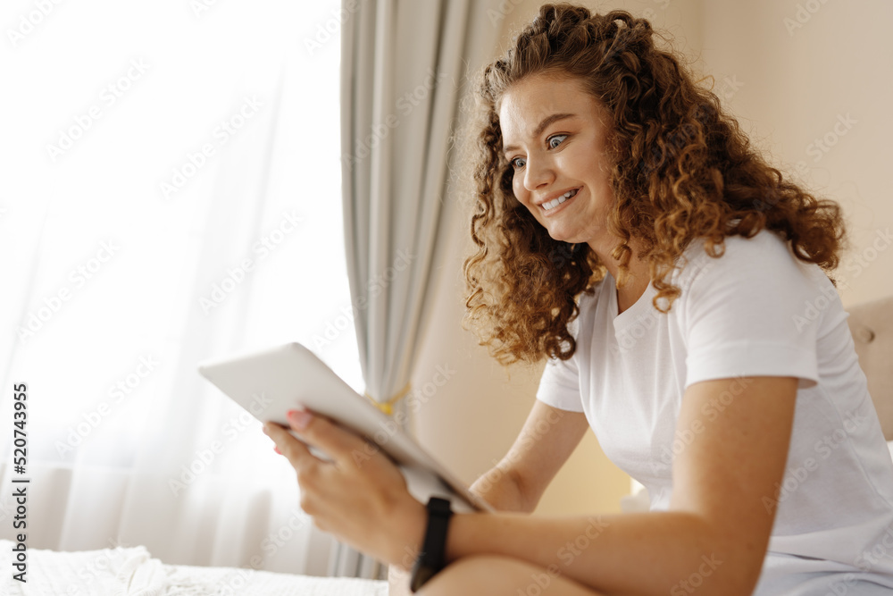 Portrait of young woman using modern digital tablet sitting on a bed