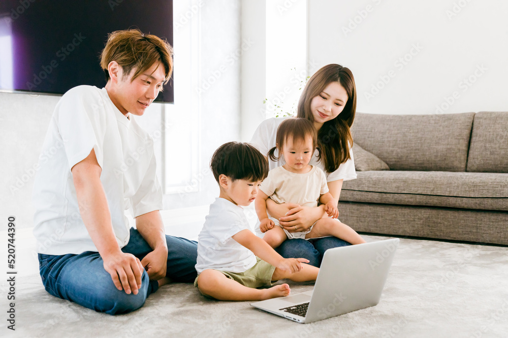 家のリビングでパソコンを使う日本人家族（子供・夫婦）
