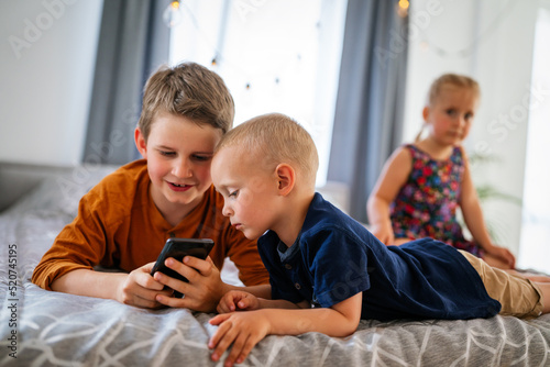 Portrait of children playing on mobile phone together at home. Internet and network addiction.