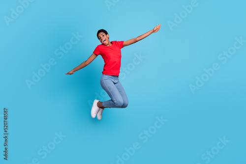 Photo of funky cheerful short hair person dressed red t-shirt jumping high arms sides isolated blue color background