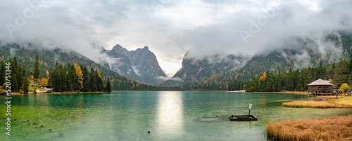 Panoramic over the Toblacher Lake Lago di Dobbiaco and Dolomite mountain summits nearby in Autumn October colors at foggy morning, Dolomites, South Tyrol, Italy. photo