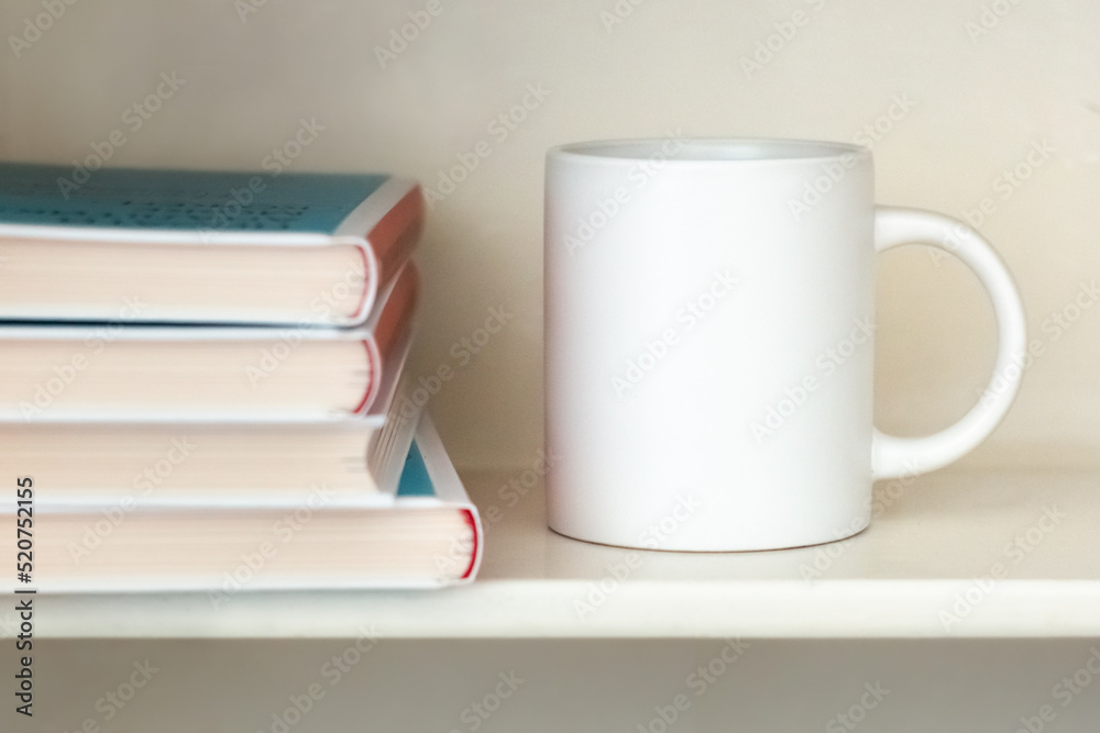 A white mug on a bookshelf near a stack of books