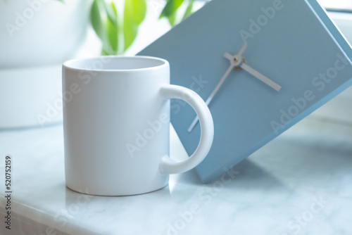 Obraz na płótnie A white mug on on the windowsill next to a modern minimalist clock w salonie