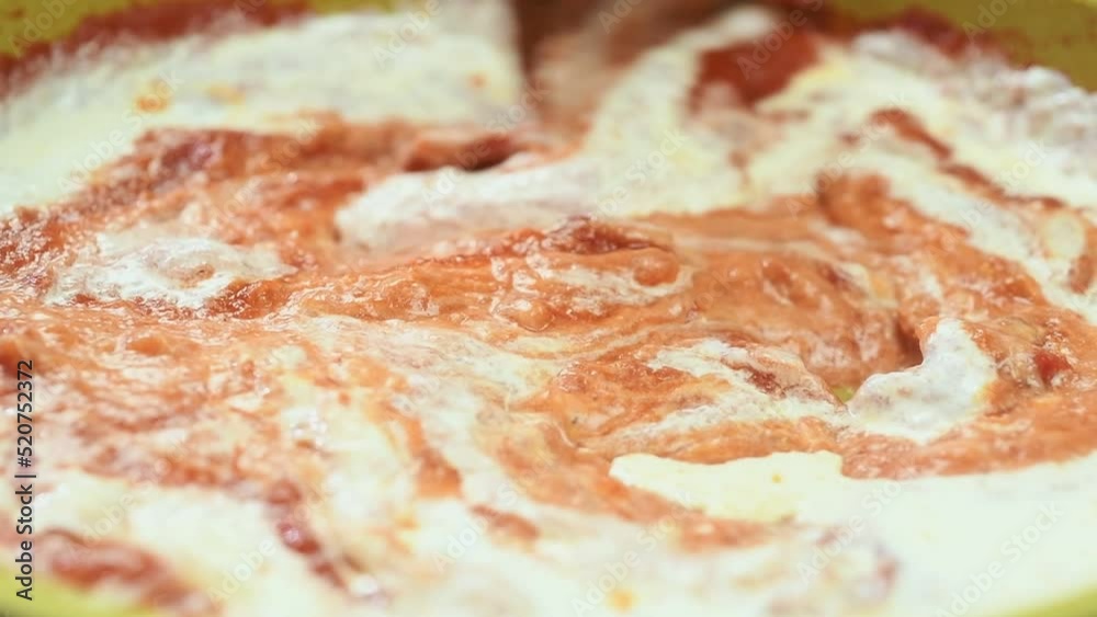 The cook stirring the tomato sauce with heavy cream in the pan.
The cook stirring the tomato sauce with heavy cream in the pan.