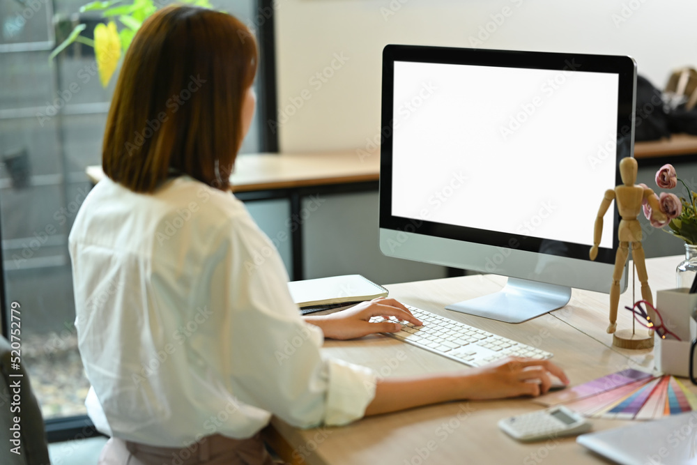 Back view of young female employee working with computer at creative office Back view of young female employee working with computer at creative office